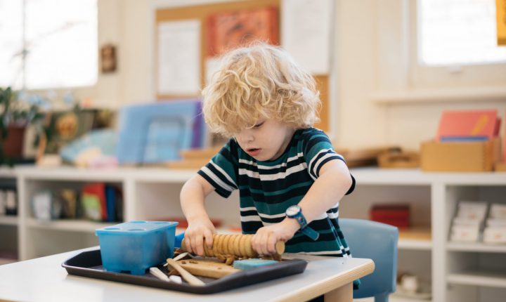 Child using rolling pin to flatten clay.